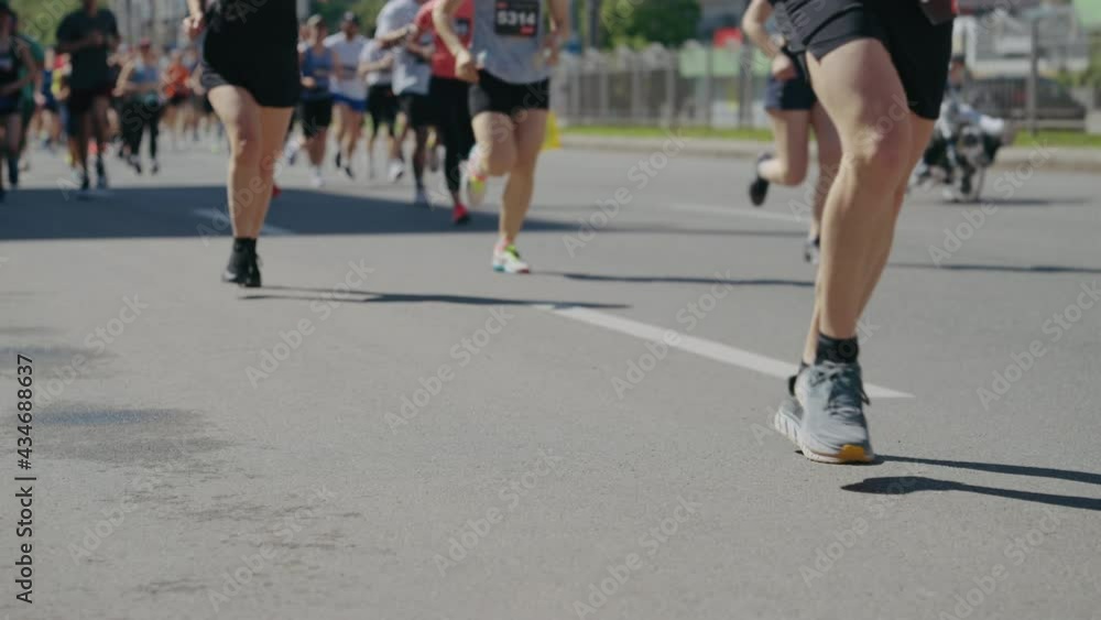 Legs of athletes running marathon on asphalt road in slow motion, focus on female legs, disabled person riding pumped wheelchair on background. Tracking shot partial view of sports event contestants Legs of athletes running marathon on asphalt road in slow motion, focus on female legs, disabled person riding pumped wheelchair on background. Tracking shot partial view of sports event contestants