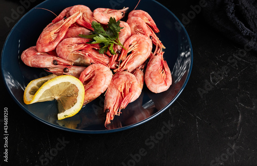 shrimp on a blue plate with lemon on a black textured background top view