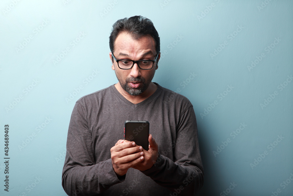 Middle aged man of Indian origin looking at his mobile phone with a surprise Middle aged man of Indian origin looking at his mobile phone with a surprise