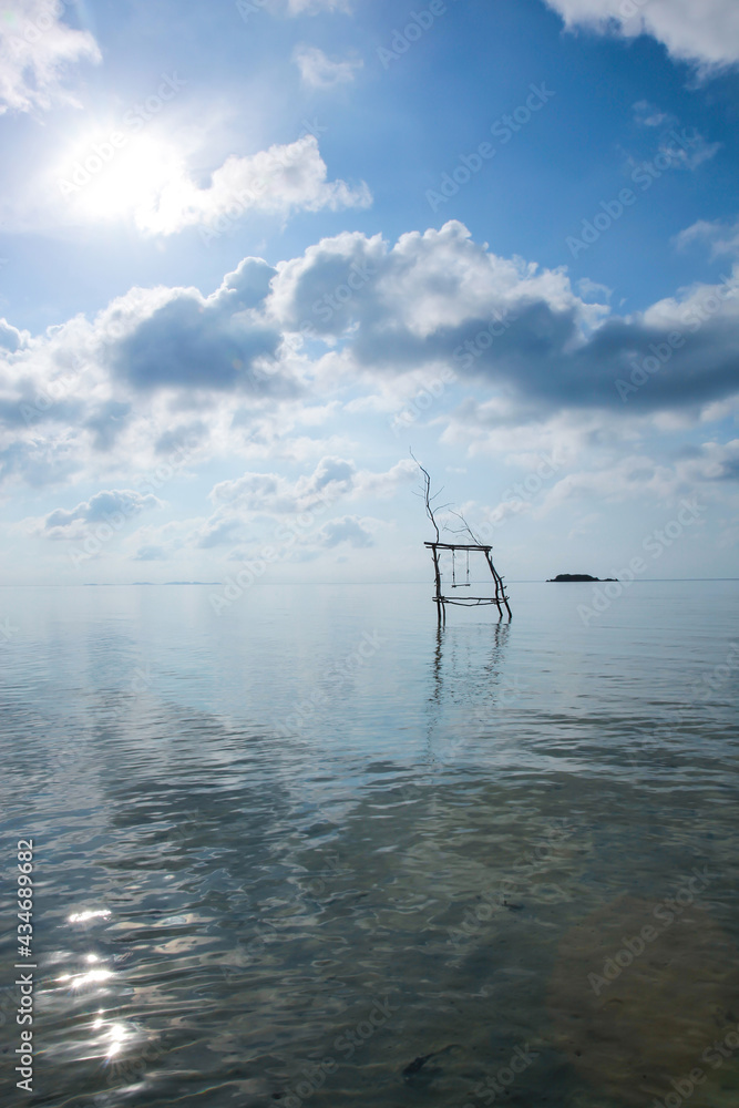 Wooden Swing over calm sea water at Karimun Jawa island with beautiful sky and sun background