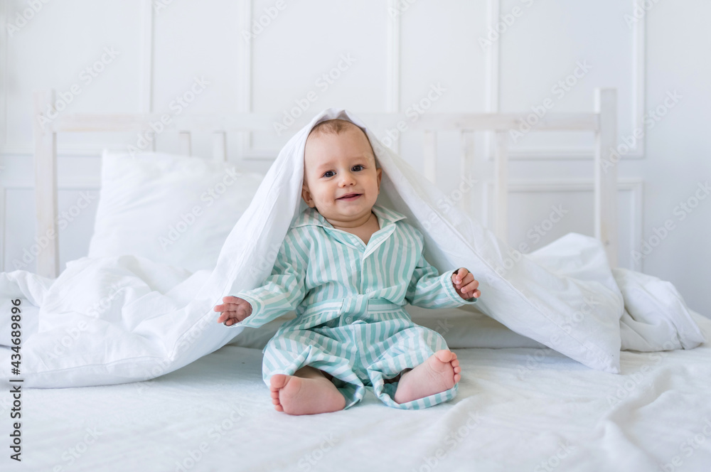 a happy toddler boy in striped pajamas sits on a bed with white linens on a white background with space for text. Morning Child a happy toddler boy in striped pajamas sits on a bed with white linens on a white background with space for text. Morning Child