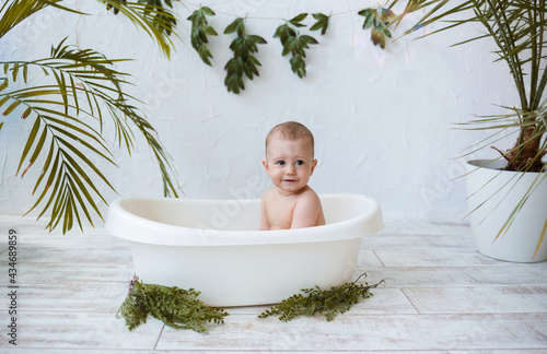 a little boy is bathing in a white bath with plants on a white background with a place for text. Water treatments for children in summer