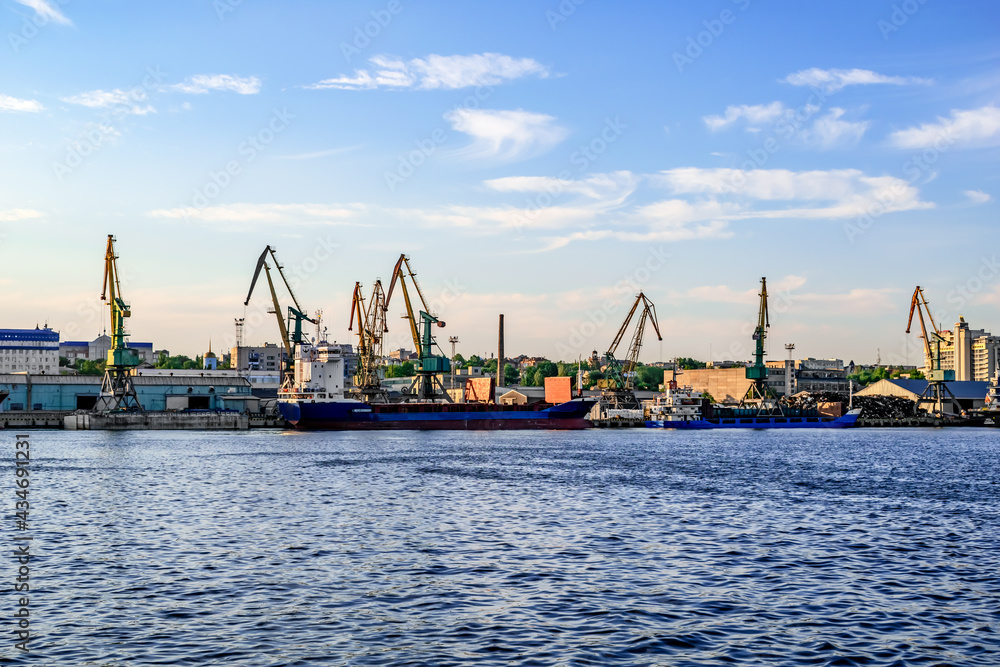 Cargo ships and harbor cranes in the Kherson river port - view from the Dnieper river (Ukraine). Water surface against the background of industrial equipment on the shore