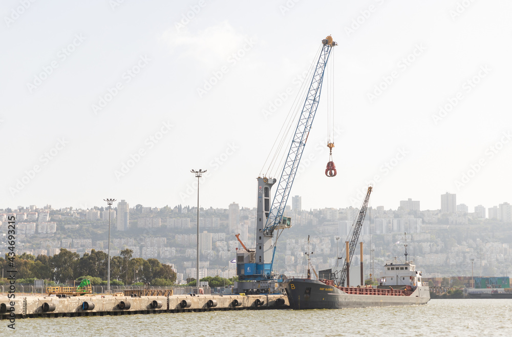 A small cargo crane unloads a cargo ship at the dock at the Haifa cargo port on the Mediterranean in Israel