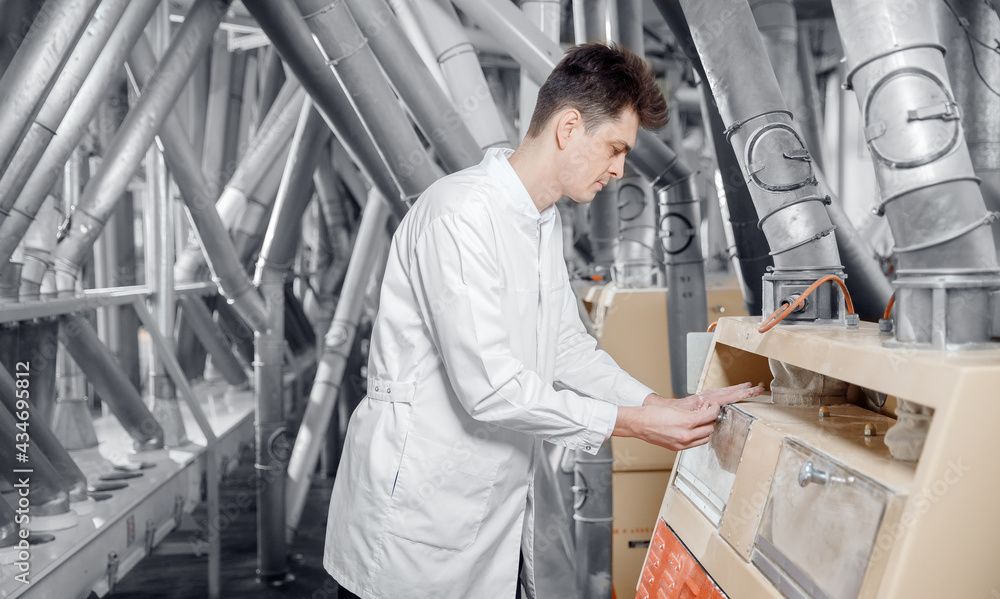 Operator checks quality of finished food products wheat flour. Modern electrical mill machinery for production Operator checks quality of finished food products wheat flour. Modern electrical mill machinery for production