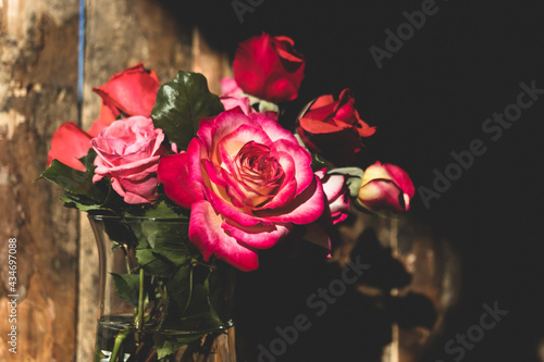 Roses of various colors standing in a vase isolated against natural light and old wood background.