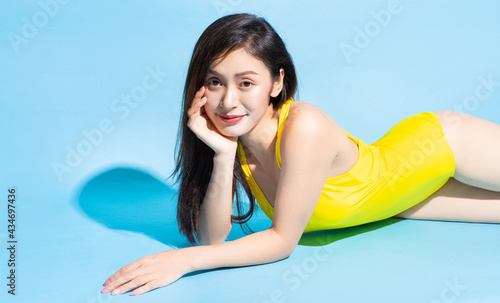 Beautiful young Asian woman in yellow swimsuit posing on blue background