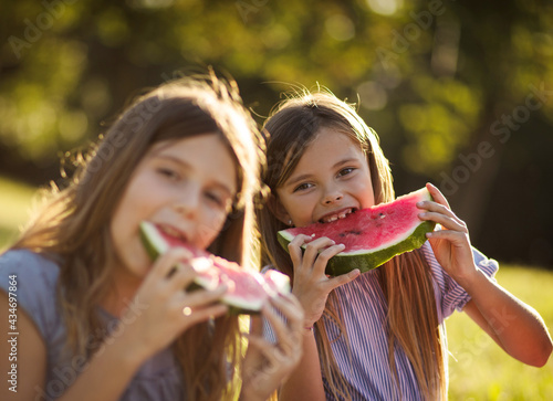  Two little girls spending time outside and eating watermelon. Focus is on background.