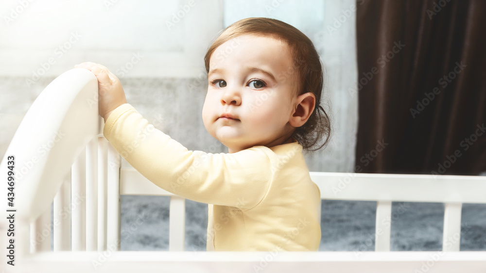 Cute little baby 8 months old standing in crib at home. looks at the camera, baby's morning, baby products concept Cute little baby 8 months old standing in crib at home. looks at the camera, baby's morning, baby products concept