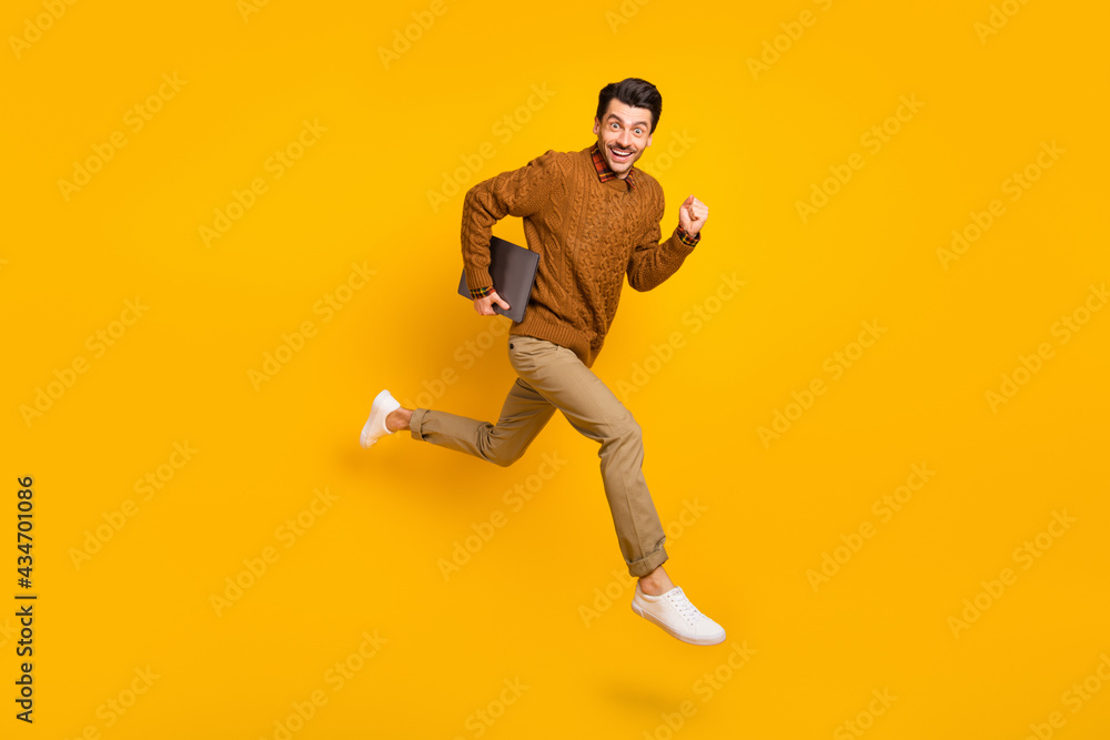 Full size profile photo of impressed nice brunet man hold laptop run wear sweater isolated on yellow background Full size profile photo of impressed nice brunet man hold laptop run wear sweater isolated on yellow background