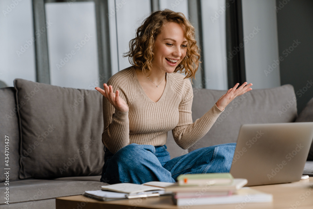 Young white woman gesturing and using laptop while sitting on couch Young white woman gesturing and using laptop while sitting on couch