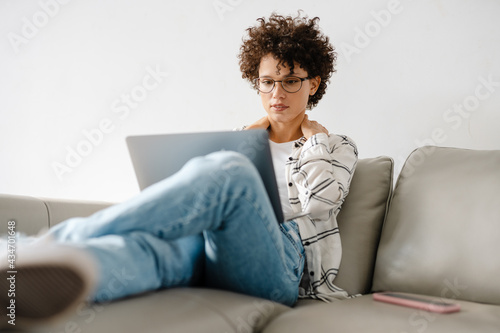 Young curly woman using laptop while sitting on couch at home