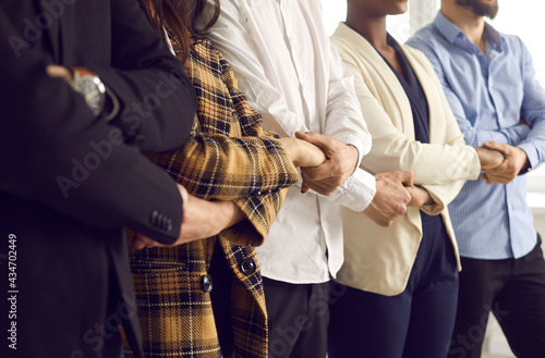 Cropped shot of diverse business team standing holding hands. United young Caucasian and African American people and coworkers supporting each other. Teamwork and strong work community concepts