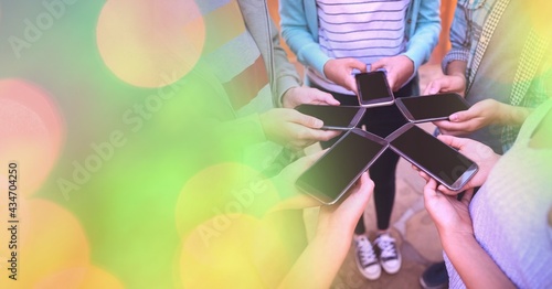 Composition of colorful light circles over diverse group of teenagers using smartphones