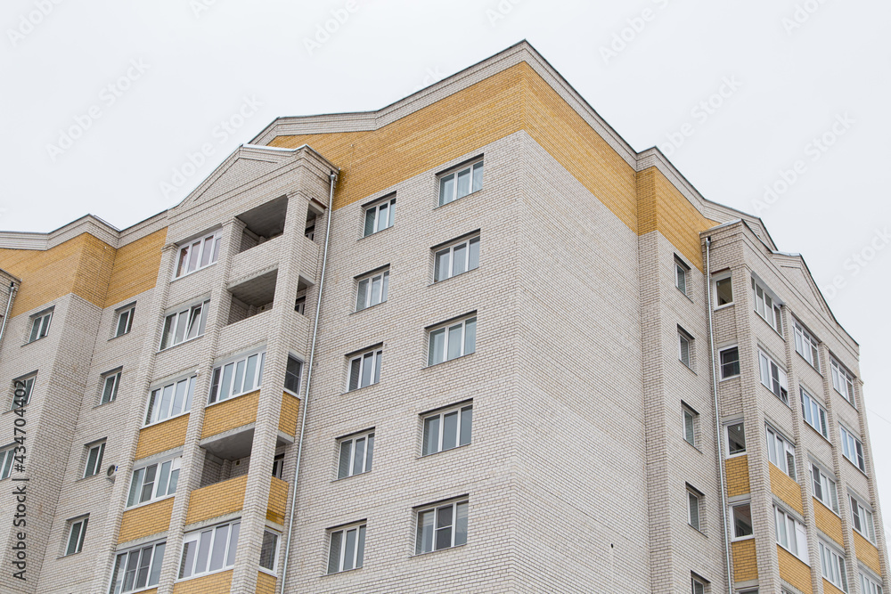 Residential high-rise building with yellow balconies and edging. Against the background of the gray sky. Modern new buildings, building facades. Real estate and urban architecture concept.