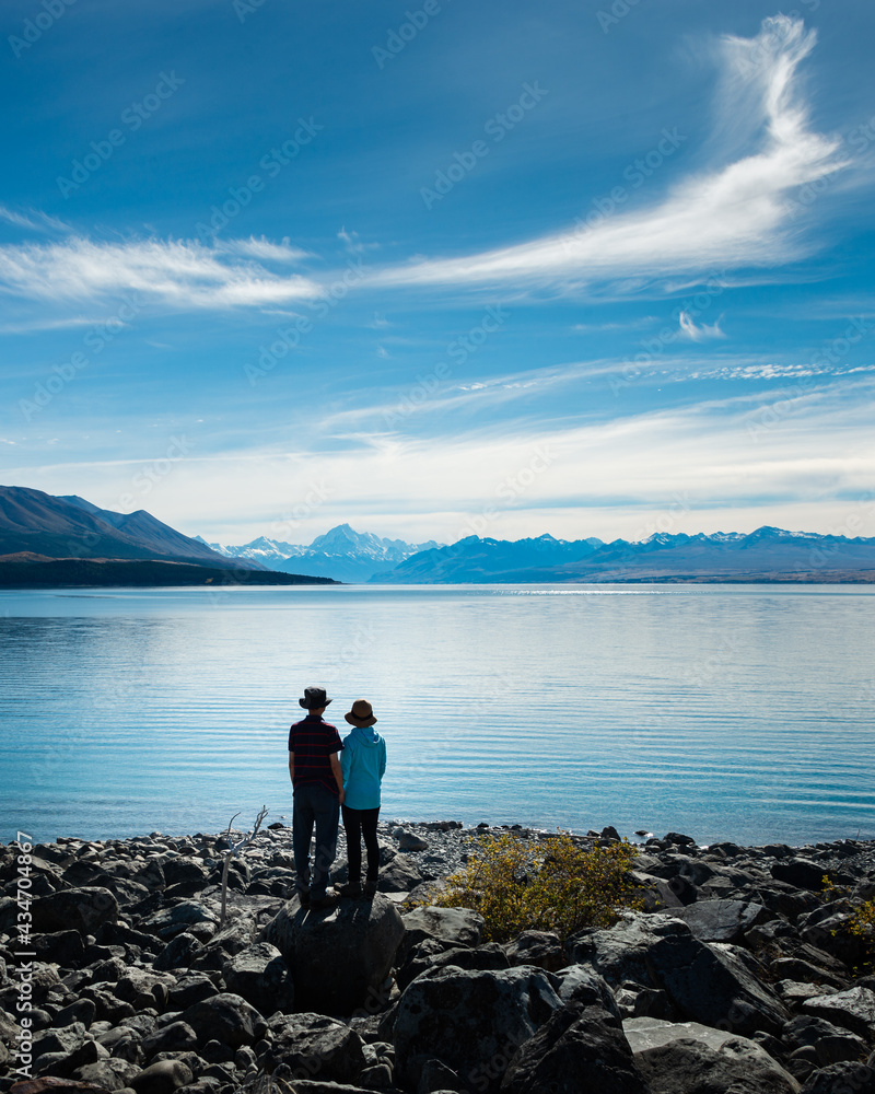 Couple standing on the shore of Lake Pukaki, enjoying the views of Mt Cook and Southern Alps, South Island. Vertical format. Couple standing on the shore of Lake Pukaki, enjoying the views of Mt Cook and Southern Alps, South Island. Vertical format.