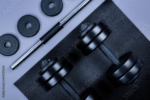 Top view of black dumbbells and different weight plates and textured mat on grey background. Flat lay. Fitness or bodybuilding sport training concept. 