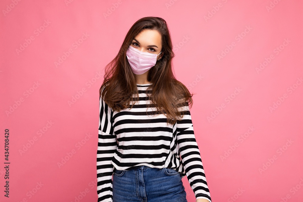 Young beautiful woman in reusable virus protective mask on face against coronavirus isolated on the pink background wall Young beautiful woman in reusable virus protective mask on face against coronavirus isolated on the pink background wall
