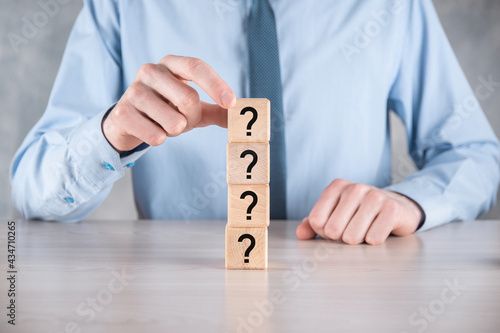 Businessman hold and put wooden cube block shape with question marks on grey table. Space for text.concept for confusion, question or solution