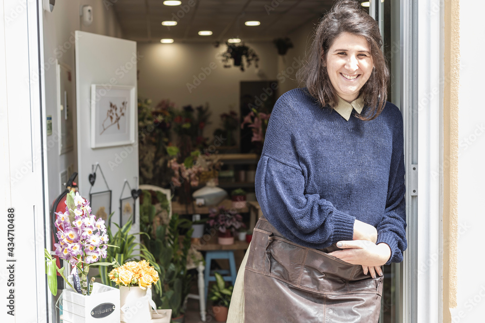 Portrait of a young cheerful woman working as florist standing at her own business shop entrance. Businesswoman concept. - obrazy, fototapety, plakaty 