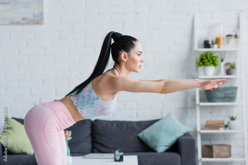 side view of brunette woman in sportswear doing forward bend exercise with outstretched hands side view of brunette woman in sportswear doing forward bend exercise with outstretched hands