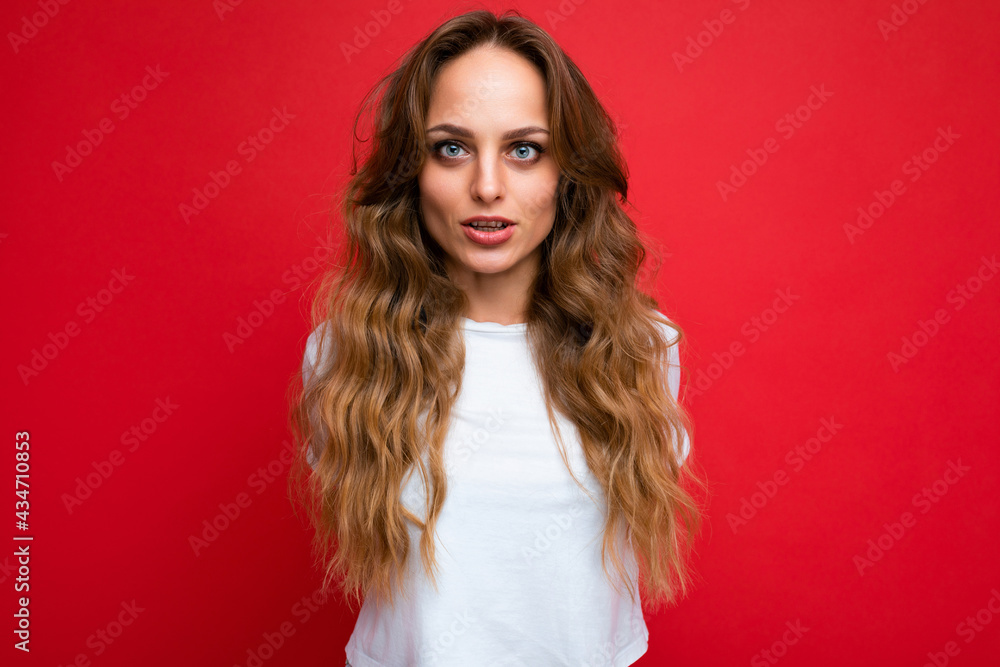 Photo of young attractive european fashion blonde woman wearing white t-shirt isolated over red background with copy space with serious expression on face. Simple and natural female person Photo of young attractive european fashion blonde woman wearing white t-shirt isolated over red background with copy space with serious expression on face. Simple and natural female person