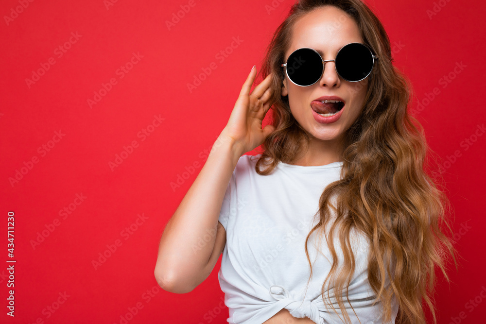Naklejka premium Photo shot of beautiful sexy young blonde woman wearing casual clothes and stylish sunglasses isolated over colorful background looking at camera