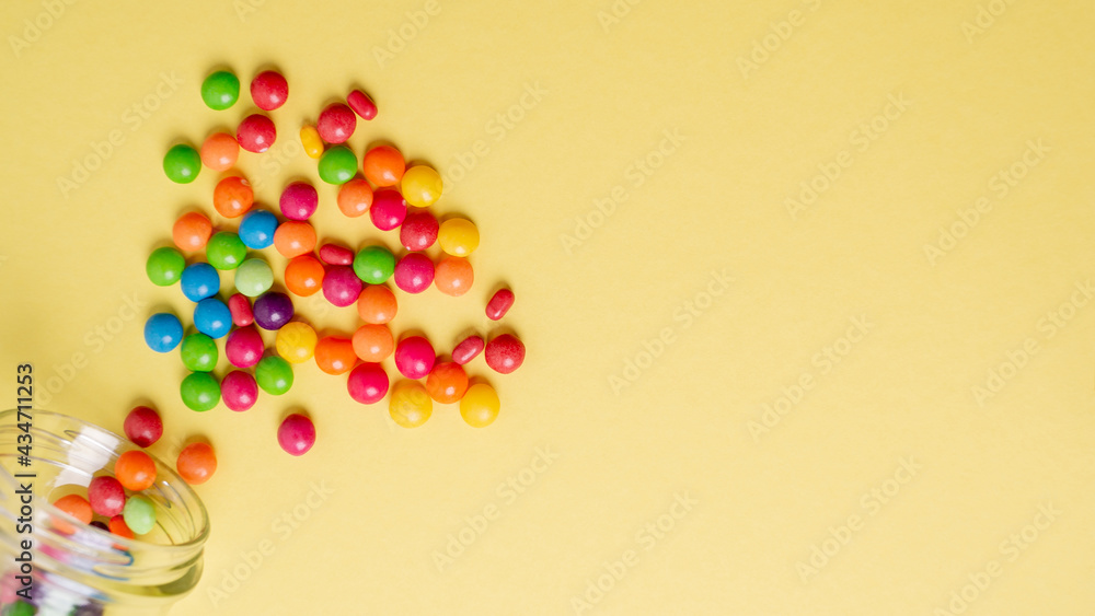 colorful candies poured from a glass jar on a colored background colorful candies poured from a glass jar on a colored background