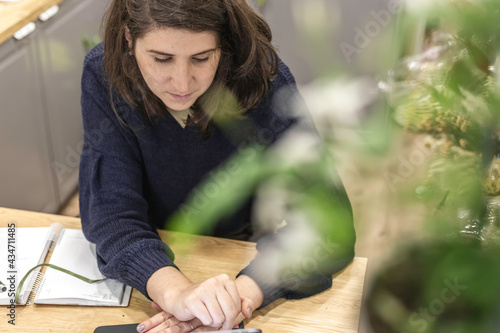 View of a cheerful young woman working as florist scheduling meeting on agenda in front of a small laptop, businesswoman concept.