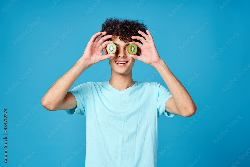 Cheerful guy with curly hair kiwi fruit blue background Cheerful guy with curly hair kiwi fruit blue background