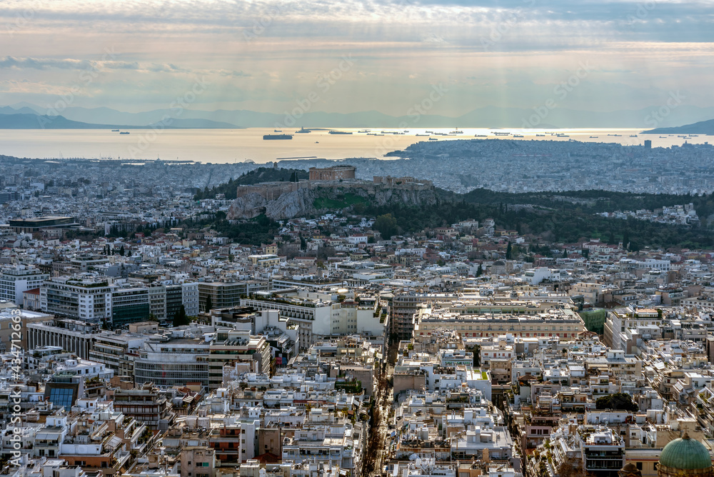 Panoramic view of the Attica basin at sunset as seen from Lycabettus hill. Acropolis with Parthenon temple, ships moored out Piraeus port, Sun rays through the cloudy sky light the Attica basin