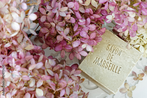 Natural soap with French language text (translate: Soap from Marseille) among pink flowers. Traditional soap from France.
