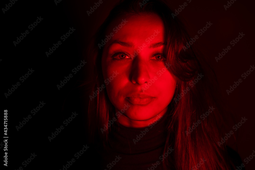Young pretty woman looks at camera in contrast red light. Sensual female person posing in dark studio with red neon lightning. Portrait of calm woman, abuse addiction, depression, imprisonment concept