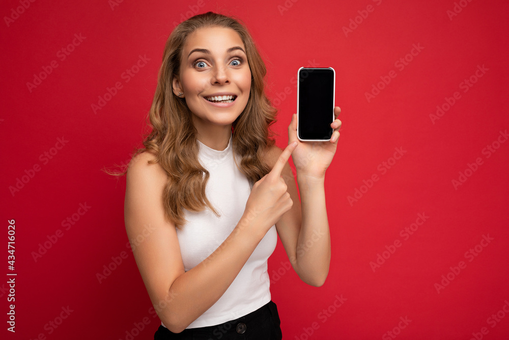 Photo of beautiful smiling young woman good looking wearing casual stylish outfit standing isolated on background with copy space holding smartphone showing phone in hand with empty screen display for Photo of beautiful smiling young woman good looking wearing casual stylish outfit standing isolated on background with copy space holding smartphone showing phone in hand with empty screen display for