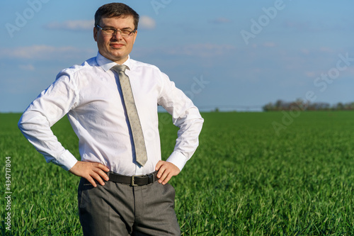 businessman poses in a field, he looks into the distance and rests, green grass and blue sky as background