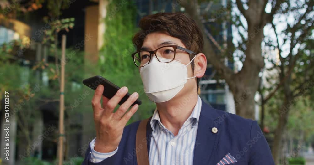Asian man wearing face mask talking on smartphone while walking on the street Asian man wearing face mask talking on smartphone while walking on the street