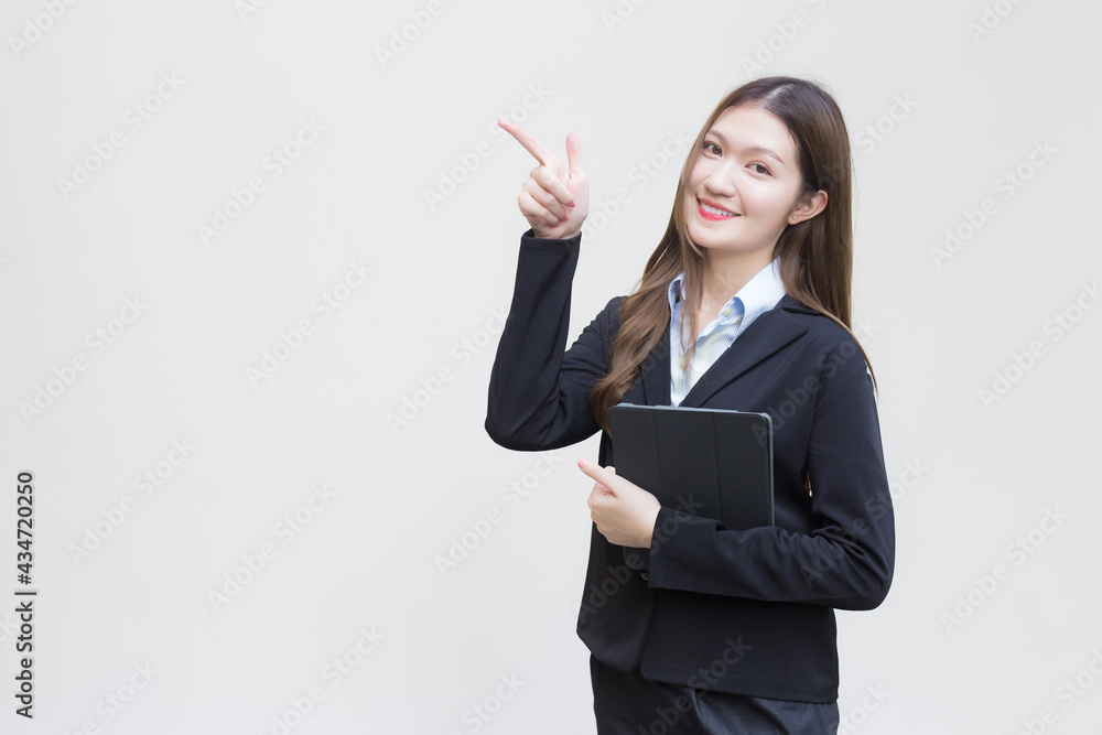Asian business working woman in black suit smiles happily while she holds tablet and shows point up to present something on white background. Asian business working woman in black suit smiles happily while she holds tablet and shows point up to present something on white background.