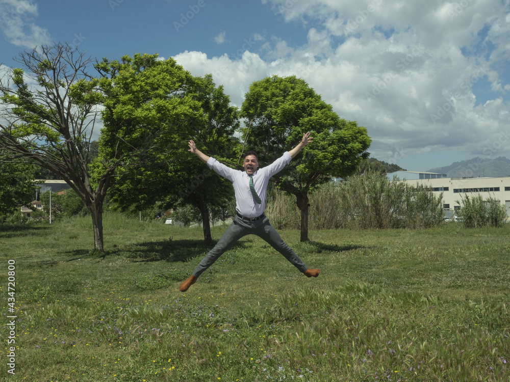 businessman jumping, in a park with green trees and has a winning, happy expression, jumping high