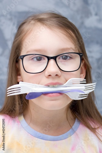 The girl has plastic cutlery and spoons in her teeth. Let`s protect the planet from disposable plastic.