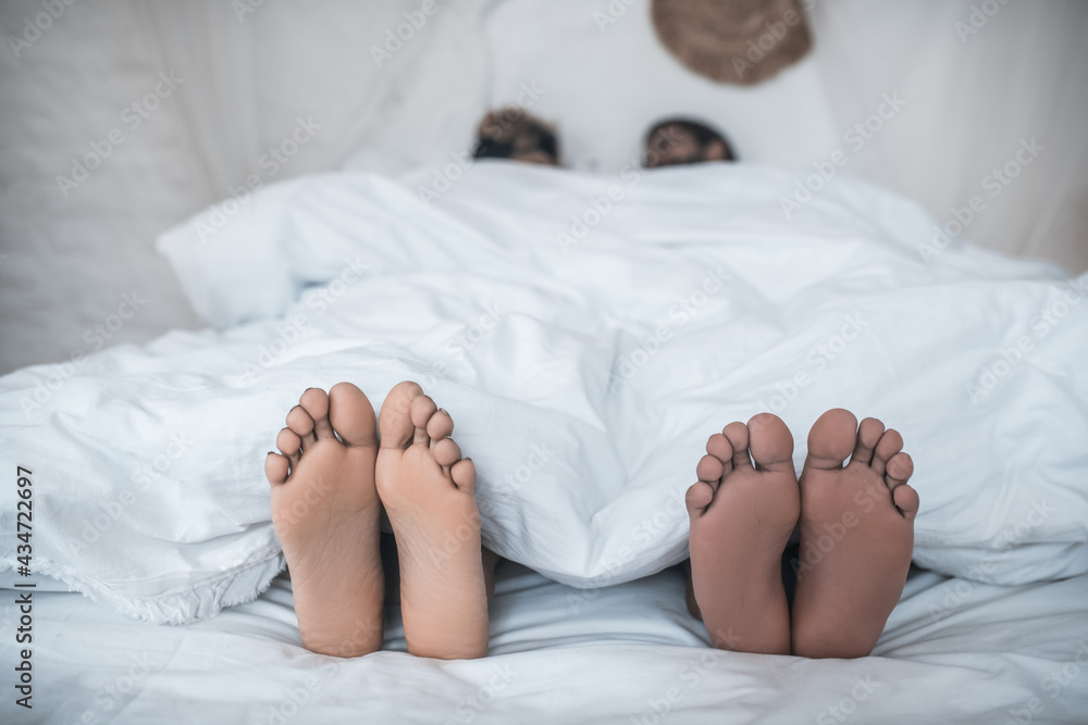 Husband and wife feet peeking out from under blanket Husband and wife feet peeking out from under blanket