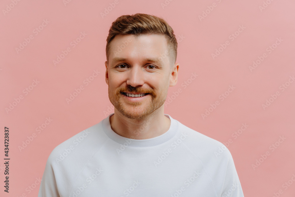 Young positive man smiling at camera in pink studio background Young positive man smiling at camera in pink studio background