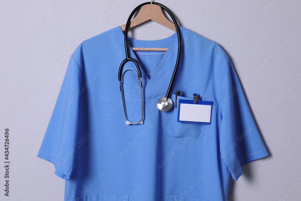 Doctor shirt with stethoscope, badge and pen hanging on light grey background Doctor shirt with stethoscope, badge and pen hanging on light grey background