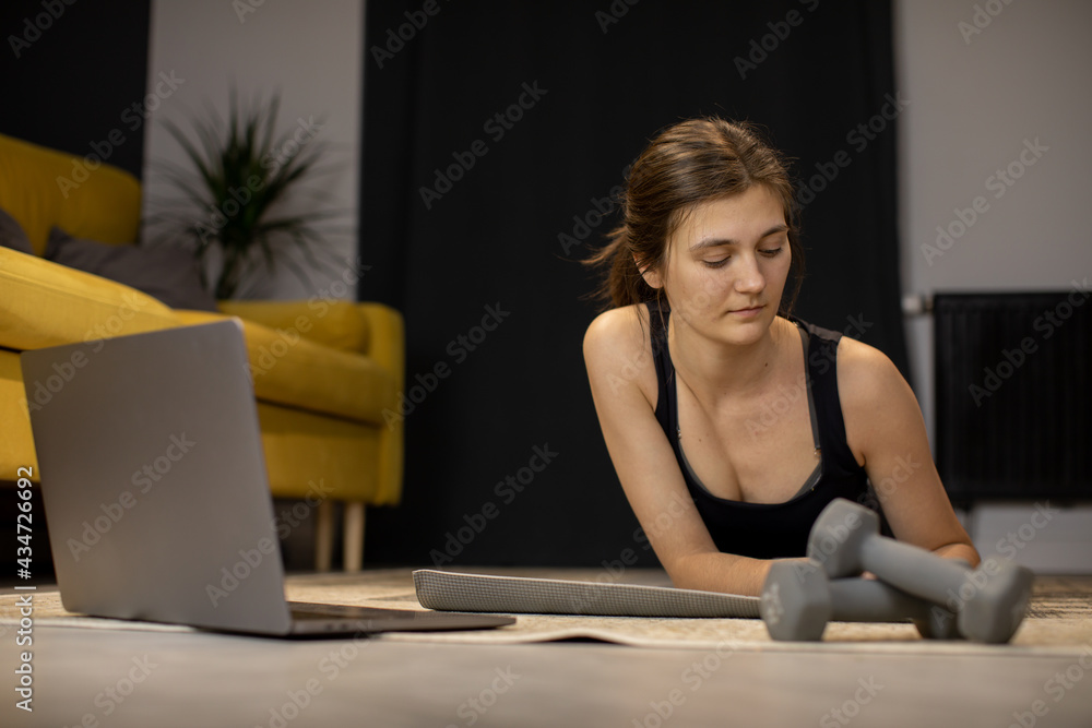 Thoughtful Lazy Girl in sportswear lying on yoga mat looking at
