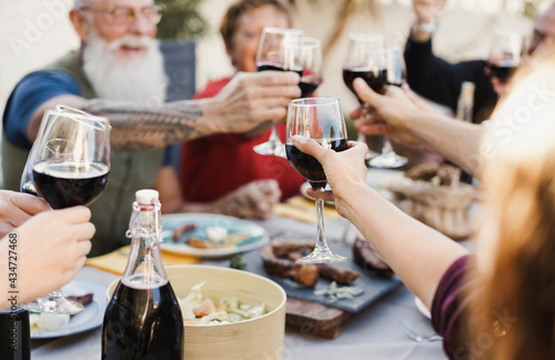 Multi generational people cheering with wine and eating outdoors at home - Focus on center hand holding glass