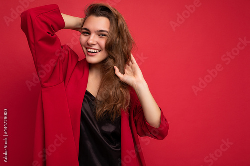Portrait of positive cheerful fashionable woman in formalwear looking at camera isolated on red background with copy space