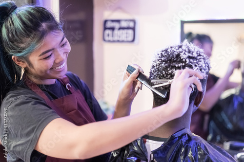 Canvas Print Young Asian woman barber  cuting black an white hair customer