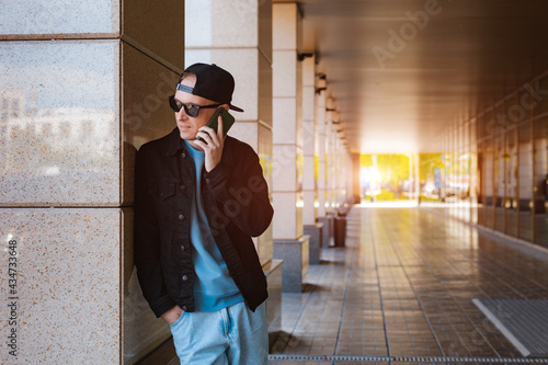 trendy stylish guy black cap sunglasses with smartphone headphones background urban urban sunset