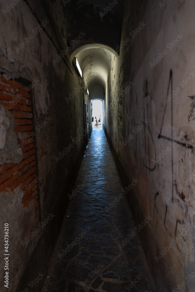 Perspective of a dark tunnel in low key. At the end of the tunnel, at the vanishing point, silhouette of people waling.
