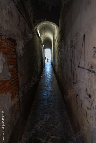 Perspective of a dark tunnel in low key. At the end of the tunnel  at the vanishing point  silhouette of people waling.