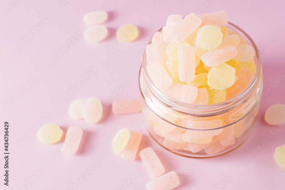 Chewing sugary citrus gummy candies in glass jar on pastel pink background. Top view, selective focus. Chewing sugary citrus gummy candies in glass jar on pastel pink background. Top view, selective focus.